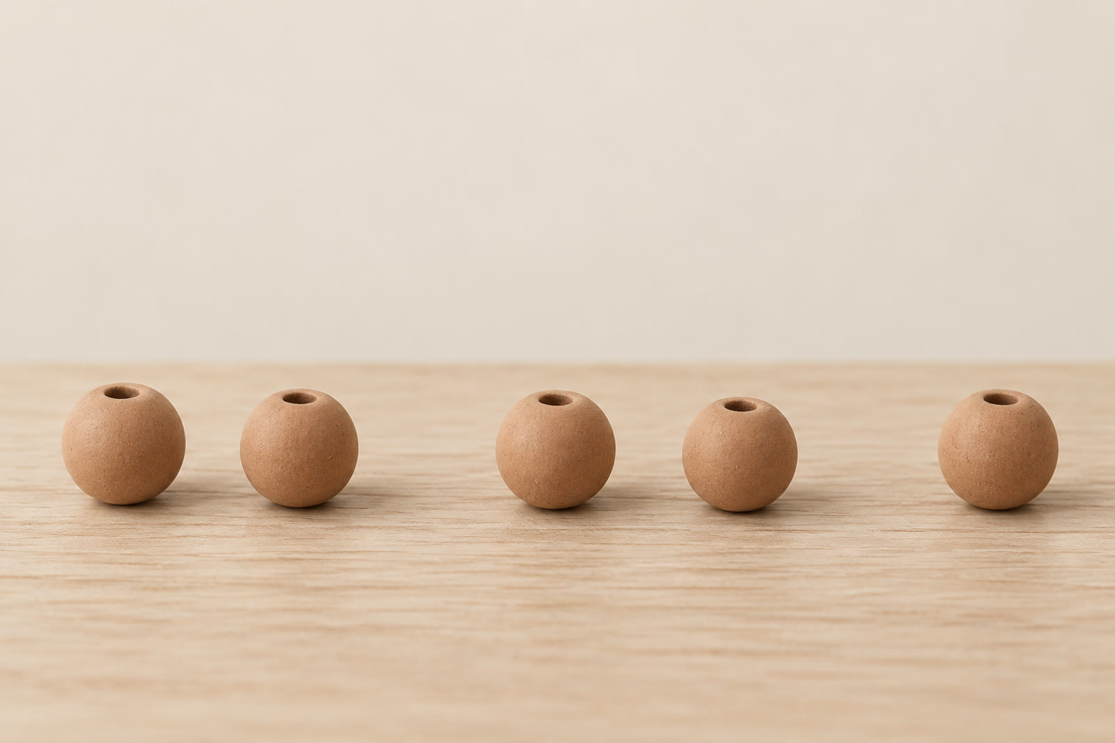 Five small clay beads resting in a row on a pale wooden surface with uneven gaps